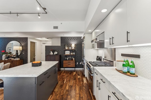 kitchen featuring wall chimney exhaust hood, white cabinetry, stainless steel stove, and tasteful backsplash