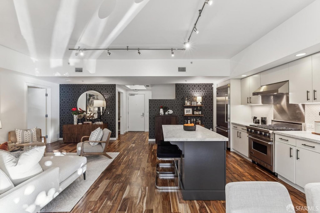 kitchen with wall chimney range hood, a kitchen island, backsplash, high quality appliances, and white cabinets