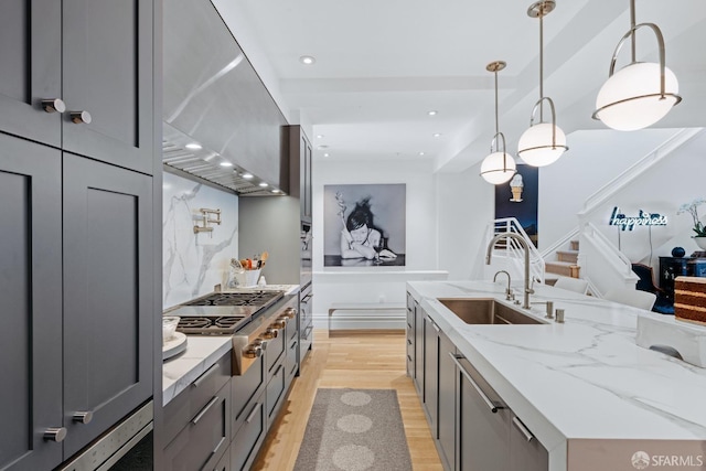 kitchen featuring sink, light stone counters, appliances with stainless steel finishes, pendant lighting, and range hood