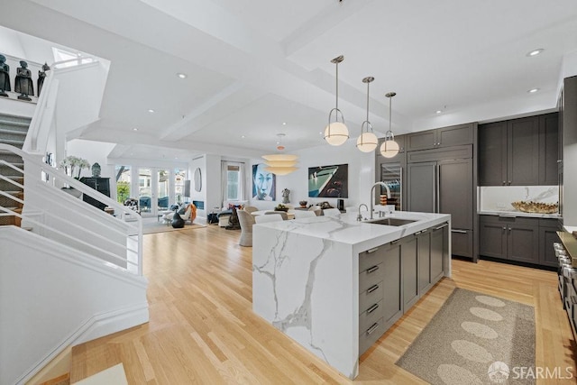 kitchen with pendant lighting, sink, paneled built in fridge, light stone countertops, and a center island with sink