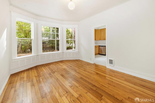 spare room with crown molding, a healthy amount of sunlight, and light wood-type flooring