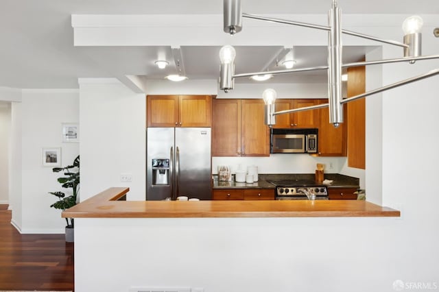 kitchen with stainless steel appliances, dark countertops, brown cabinetry, and dark wood finished floors