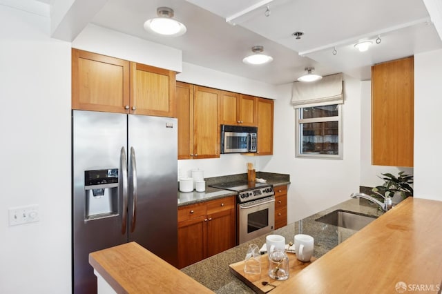 kitchen with appliances with stainless steel finishes, brown cabinetry, a sink, and a peninsula