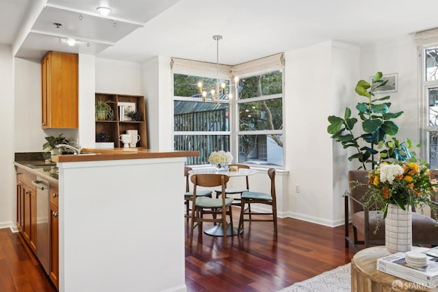 kitchen featuring dark wood finished floors, decorative light fixtures, a peninsula, a sink, and a notable chandelier