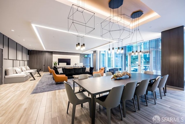 dining space featuring an inviting chandelier, a tray ceiling, floor to ceiling windows, and light wood-style flooring