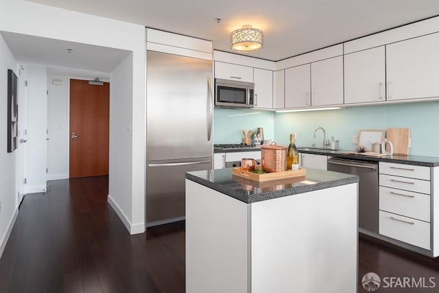 kitchen with a kitchen island, a sink, dark wood-type flooring, appliances with stainless steel finishes, and white cabinetry