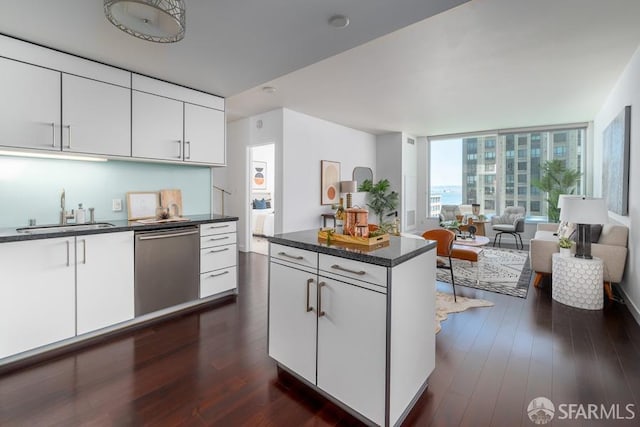 kitchen featuring dark wood-style floors, white cabinetry, a sink, stainless steel dishwasher, and a center island