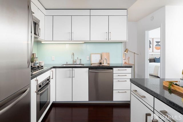 kitchen featuring white cabinets, stainless steel appliances, dark stone counters, and a sink