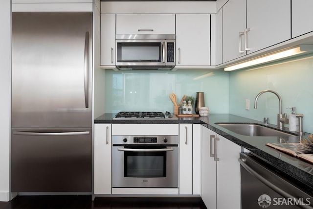 kitchen featuring a sink, stainless steel appliances, white cabinets, dark countertops, and tasteful backsplash