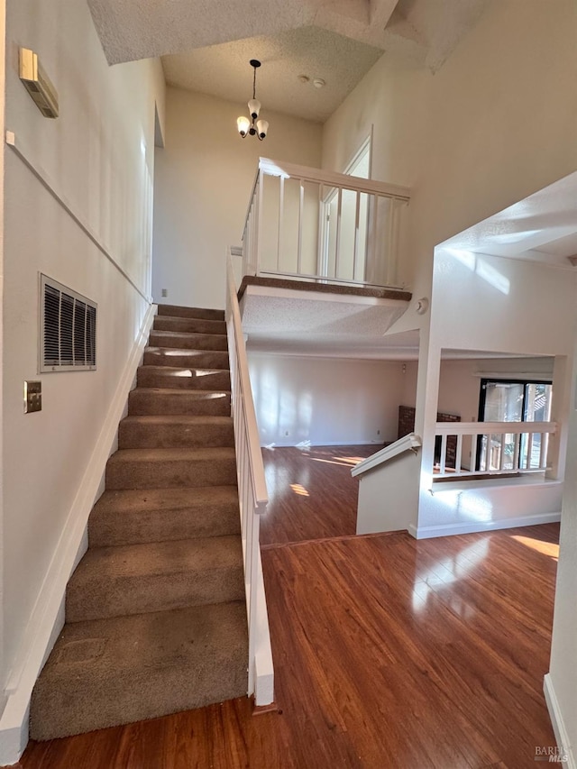 stairs with an inviting chandelier, a healthy amount of sunlight, hardwood / wood-style floors, and a high ceiling