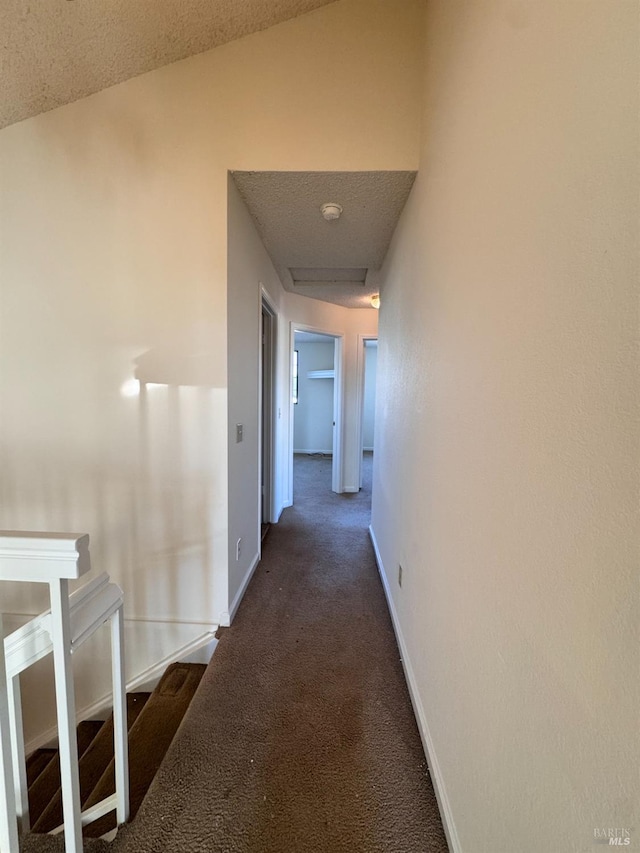 corridor with dark carpet and a textured ceiling