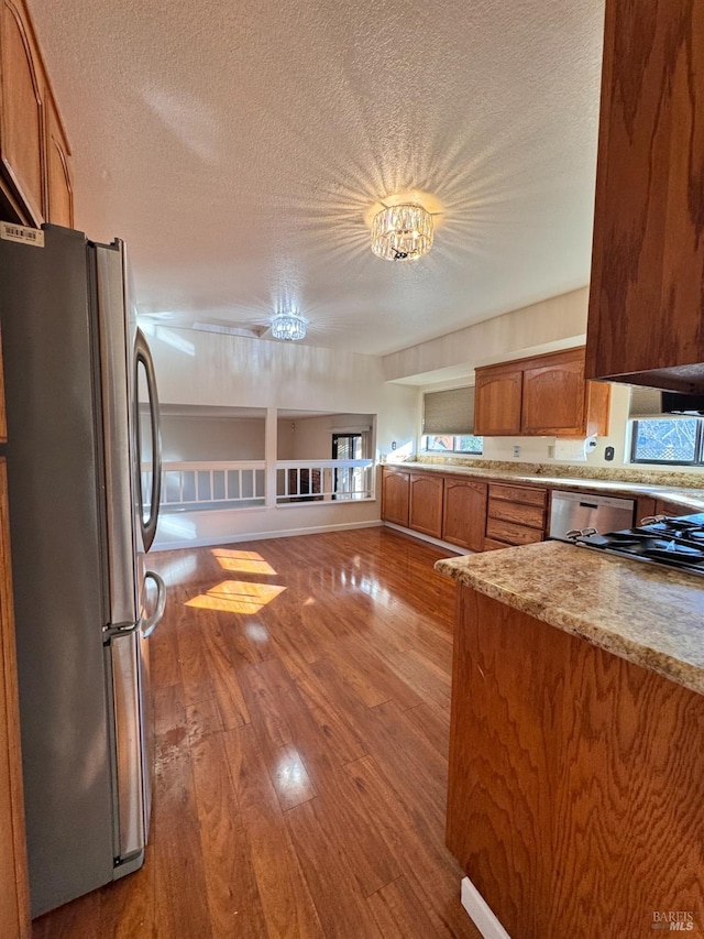 kitchen with light stone counters, stainless steel fridge, a textured ceiling, and light wood-type flooring