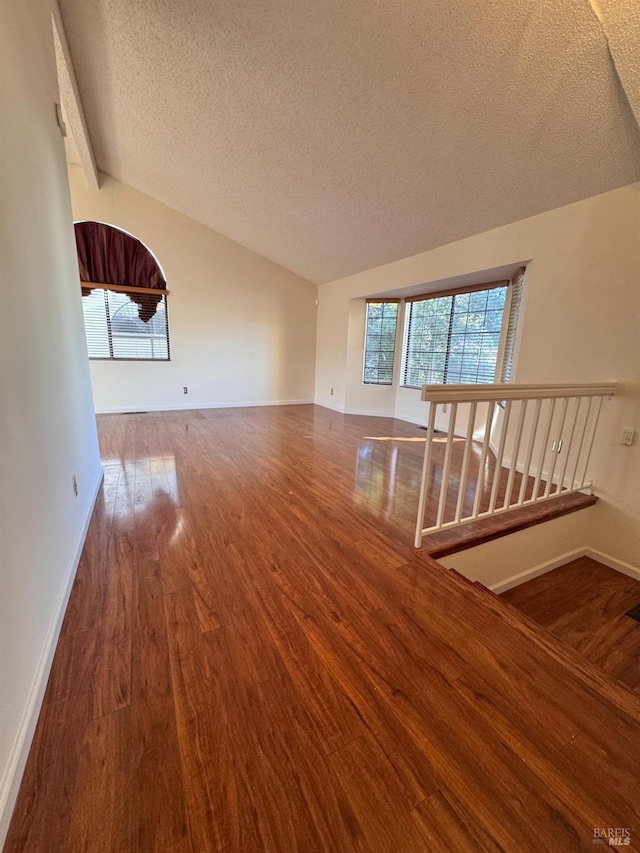 empty room with wood-type flooring, vaulted ceiling, and a textured ceiling