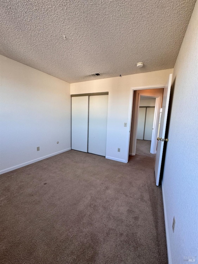 unfurnished bedroom with dark carpet, a closet, and a textured ceiling