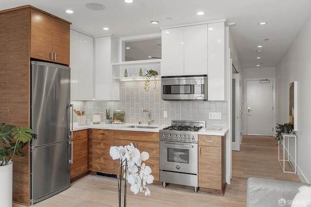 kitchen featuring sink, light hardwood / wood-style flooring, appliances with stainless steel finishes, tasteful backsplash, and white cabinets