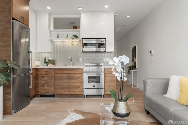 kitchen featuring tasteful backsplash, stainless steel appliances, light hardwood / wood-style floors, and white cabinets