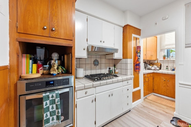 kitchen featuring light wood-type flooring, under cabinet range hood, stainless steel appliances, and backsplash