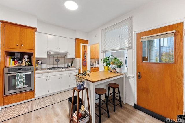 kitchen with tasteful backsplash, stainless steel appliances, light wood-type flooring, under cabinet range hood, and white cabinetry