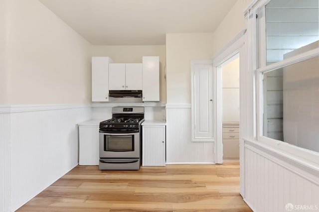 kitchen with stainless steel range with gas cooktop, light wood-style floors, wainscoting, white cabinetry, and under cabinet range hood