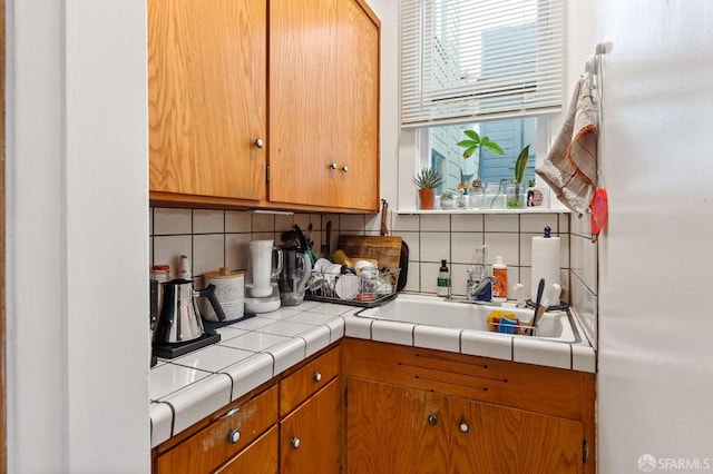 kitchen with brown cabinetry, a sink, tile counters, and decorative backsplash