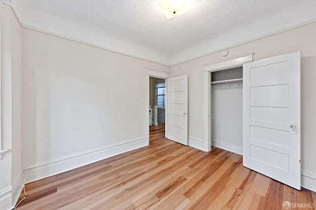 unfurnished bedroom featuring light wood finished floors, a closet, baseboards, and a textured ceiling