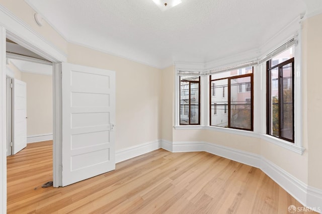 spare room with light wood-style flooring, baseboards, and a textured ceiling