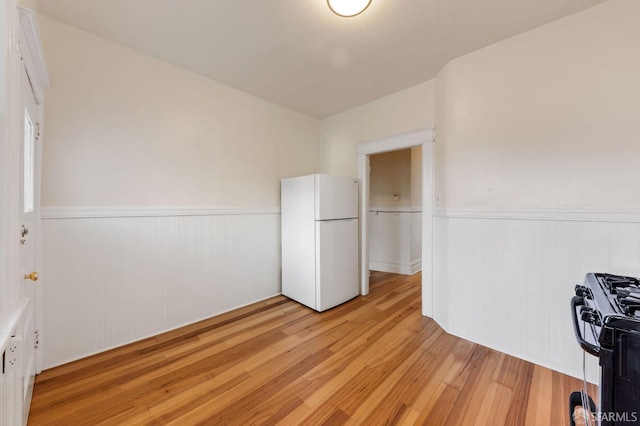 interior space with light wood-type flooring, freestanding refrigerator, wainscoting, and black gas stove