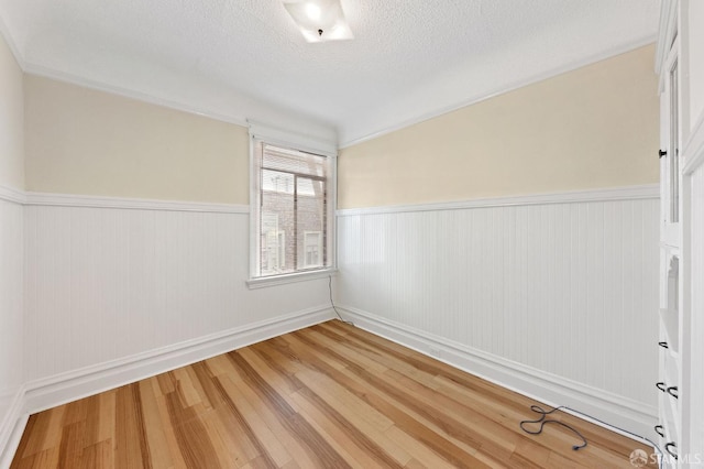 spare room with a wainscoted wall, a textured ceiling, and hardwood / wood-style floors