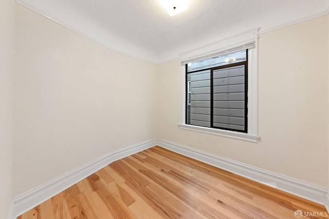 empty room with a textured ceiling, light wood finished floors, and baseboards