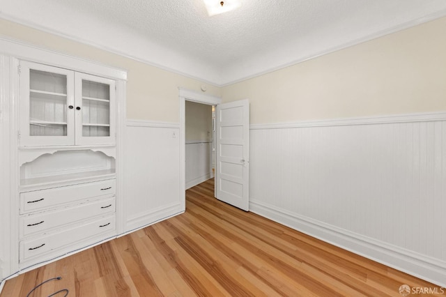 unfurnished bedroom featuring light wood-type flooring, a wainscoted wall, and a textured ceiling