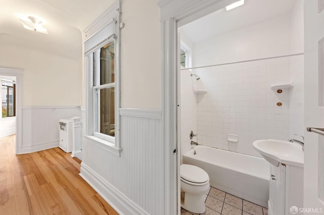 bathroom with toilet, a sink, wood finished floors, shower / bathing tub combination, and wainscoting