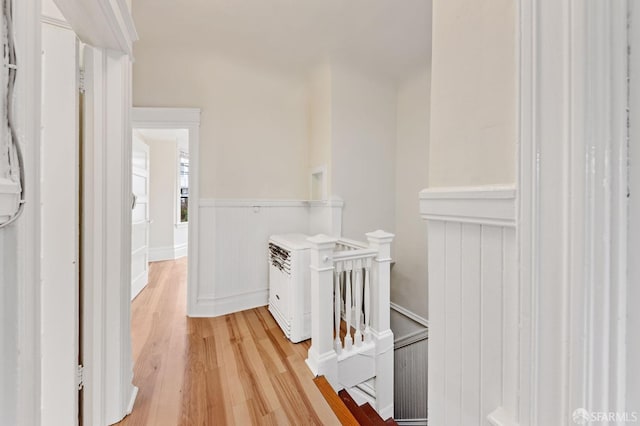 corridor with light wood finished floors, an upstairs landing, and wainscoting