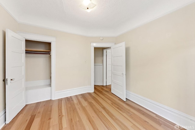 unfurnished bedroom featuring a closet, baseboards, light wood-style flooring, and a textured ceiling