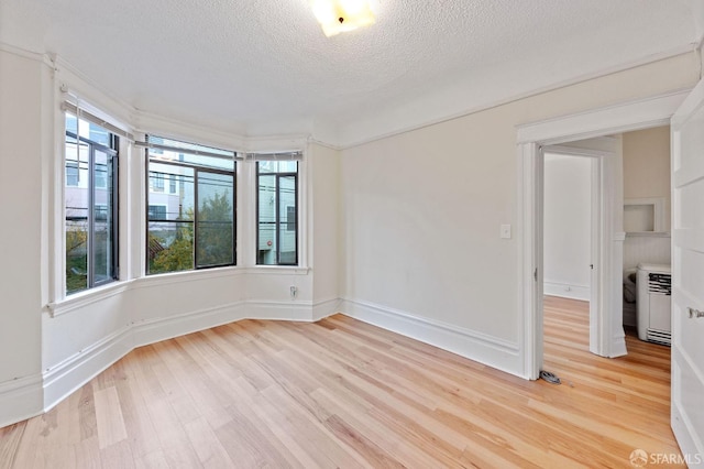 unfurnished room with a textured ceiling, plenty of natural light, light wood-style flooring, and baseboards