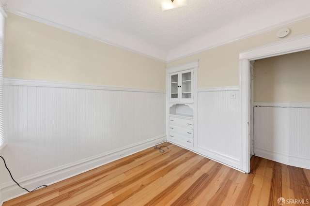 unfurnished bedroom with a wainscoted wall, a textured ceiling, and light wood-style floors