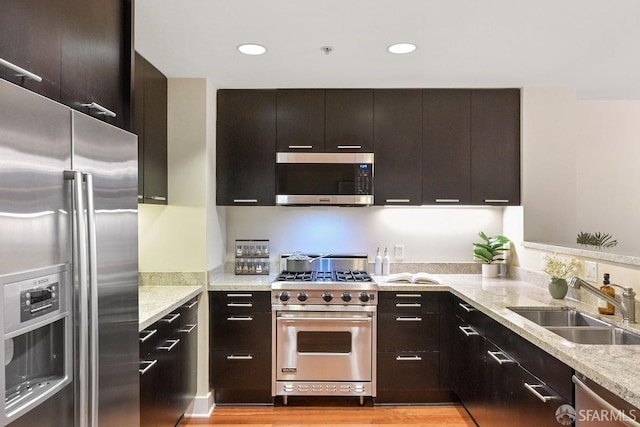 kitchen featuring appliances with stainless steel finishes, light stone countertops, dark brown cabinets, light hardwood / wood-style flooring, and sink