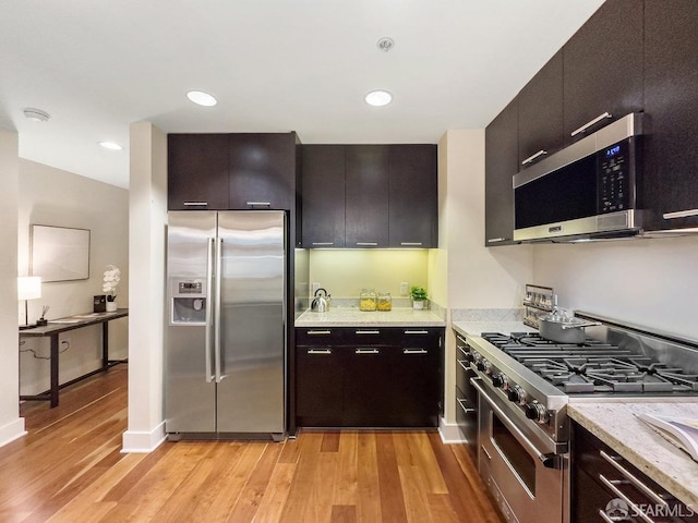 kitchen with light wood-type flooring, stainless steel appliances, and light stone counters