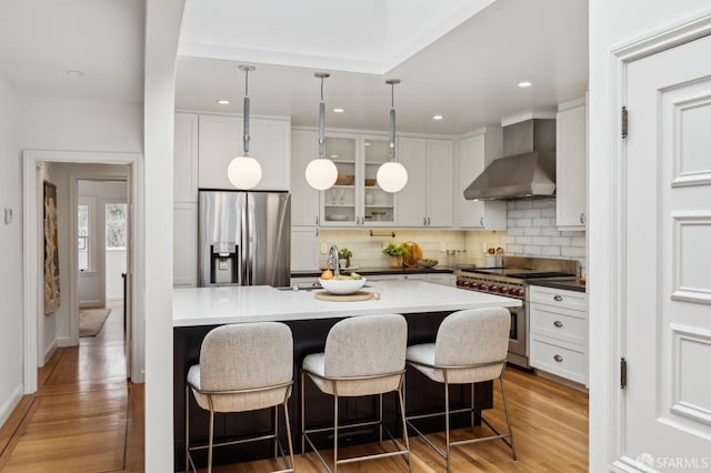 kitchen with white cabinetry, decorative light fixtures, wall chimney exhaust hood, and appliances with stainless steel finishes