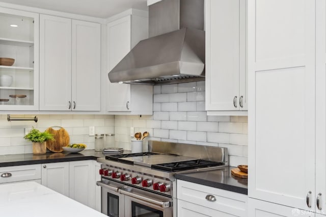 kitchen with range with two ovens, white cabinetry, tasteful backsplash, and wall chimney exhaust hood