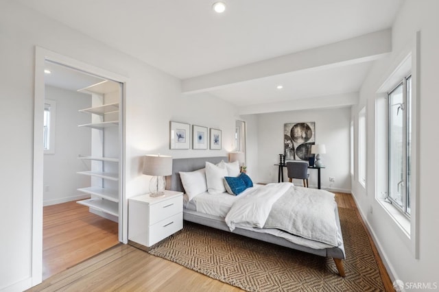 bedroom featuring beam ceiling, hardwood / wood-style floors, and multiple windows