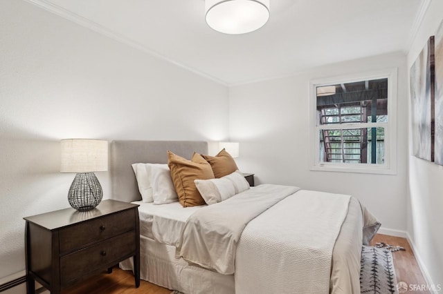 bedroom with ornamental molding, wood-type flooring, and a baseboard heating unit