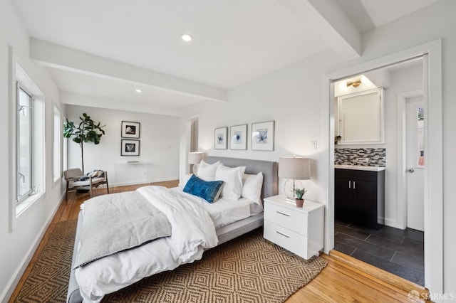 bedroom featuring ensuite bathroom, dark wood-type flooring, and beam ceiling