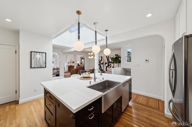 kitchen with hanging light fixtures, light wood-type flooring, an island with sink, stainless steel appliances, and white cabinets