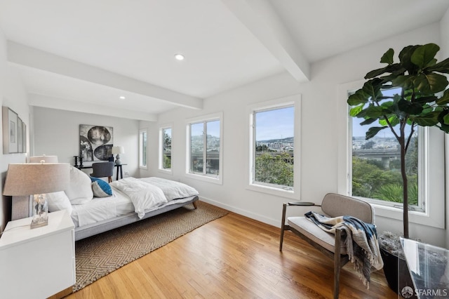 bedroom featuring multiple windows, hardwood / wood-style floors, and beam ceiling