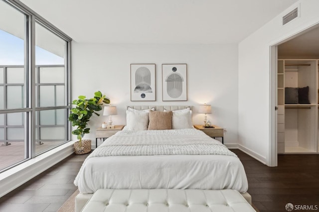 bedroom with a walk in closet, dark wood-type flooring, and expansive windows