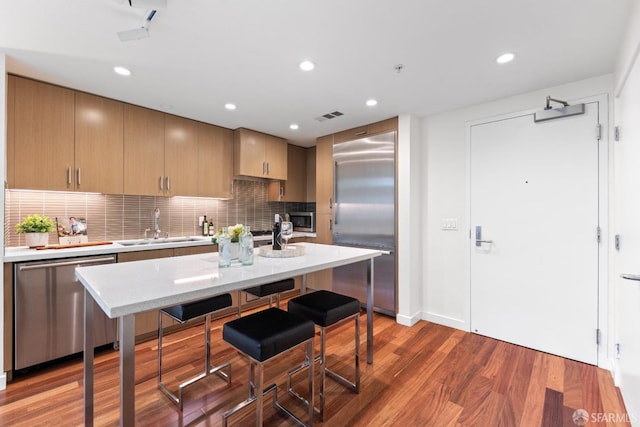 2655 Bush St Unit 119, San Francisco, CA 94115 - kitchen with appliances with stainless steel finishes, decorative backsplash, wood finished floors, a breakfast bar area, and recessed lighting