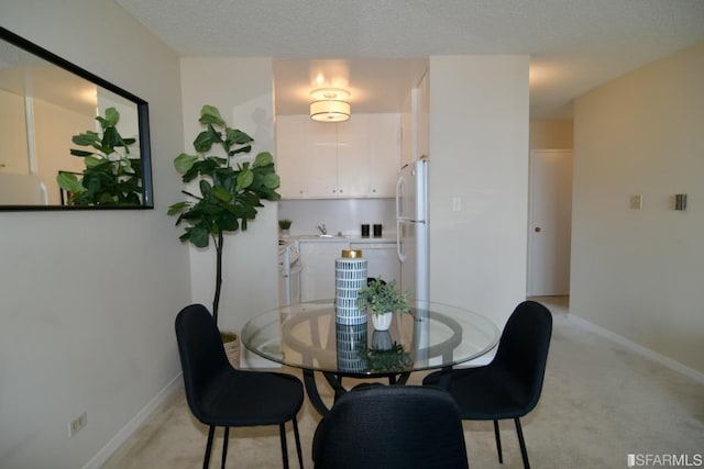 dining space featuring light colored carpet, a textured ceiling, and baseboards