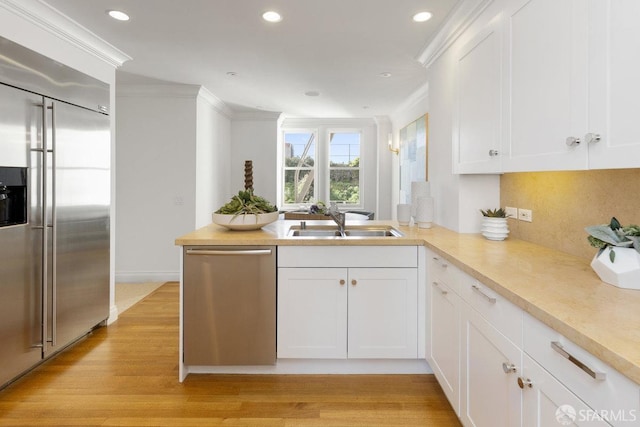 kitchen featuring white cabinets, a peninsula, stainless steel appliances, light countertops, and a sink