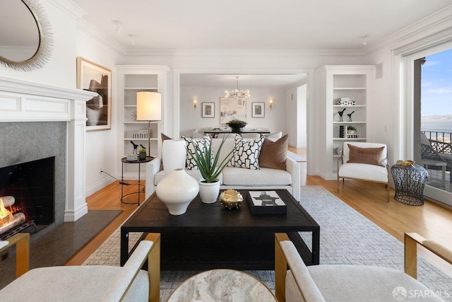 living area featuring a lit fireplace, ornamental molding, wood finished floors, and a notable chandelier