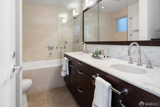 bathroom featuring toilet, double vanity, tile walls, and a sink